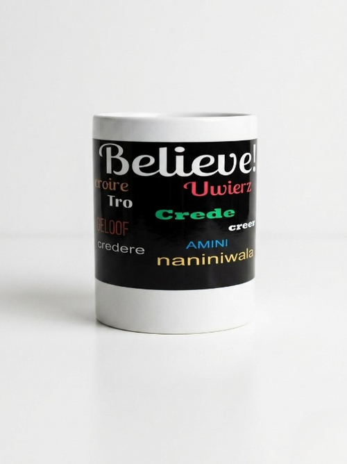 A front view of the white 11-ounce ceramic mug featuring a wide black wrap-around band. The word "Believe!" is prominently displayed at the top in large, white cursive script. Below it, the word is translated into various languages. The design is clean and inspirational, set against a bright, minimalist white background.   Shop www.ANDREAANDME.com