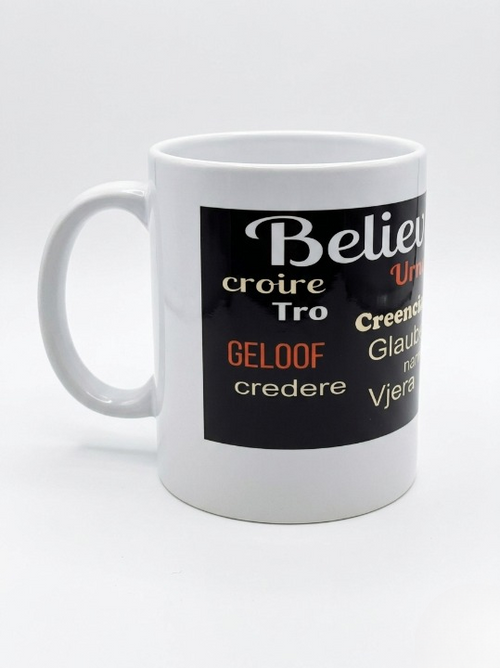 A left side view of handle of white 11-ounce ceramic mug featuring a wide black wrap-around band. The word "Believe!" is prominently displayed at the top in large, white cursive script. Below it, the word is translated into various languages. The design is clean and inspirational, set against a bright, minimalist white background.   Shop www.ANDREAANDME.com