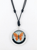 Front view of an orange and white polka dots butterfly acrylic and mixed media pendant necklace. The graphic features a close-up of the circular 2 1/2 inch pendant containing an orange butterfly with white polka dots against a black and white striped background.  Shop at www.andreaandme.com